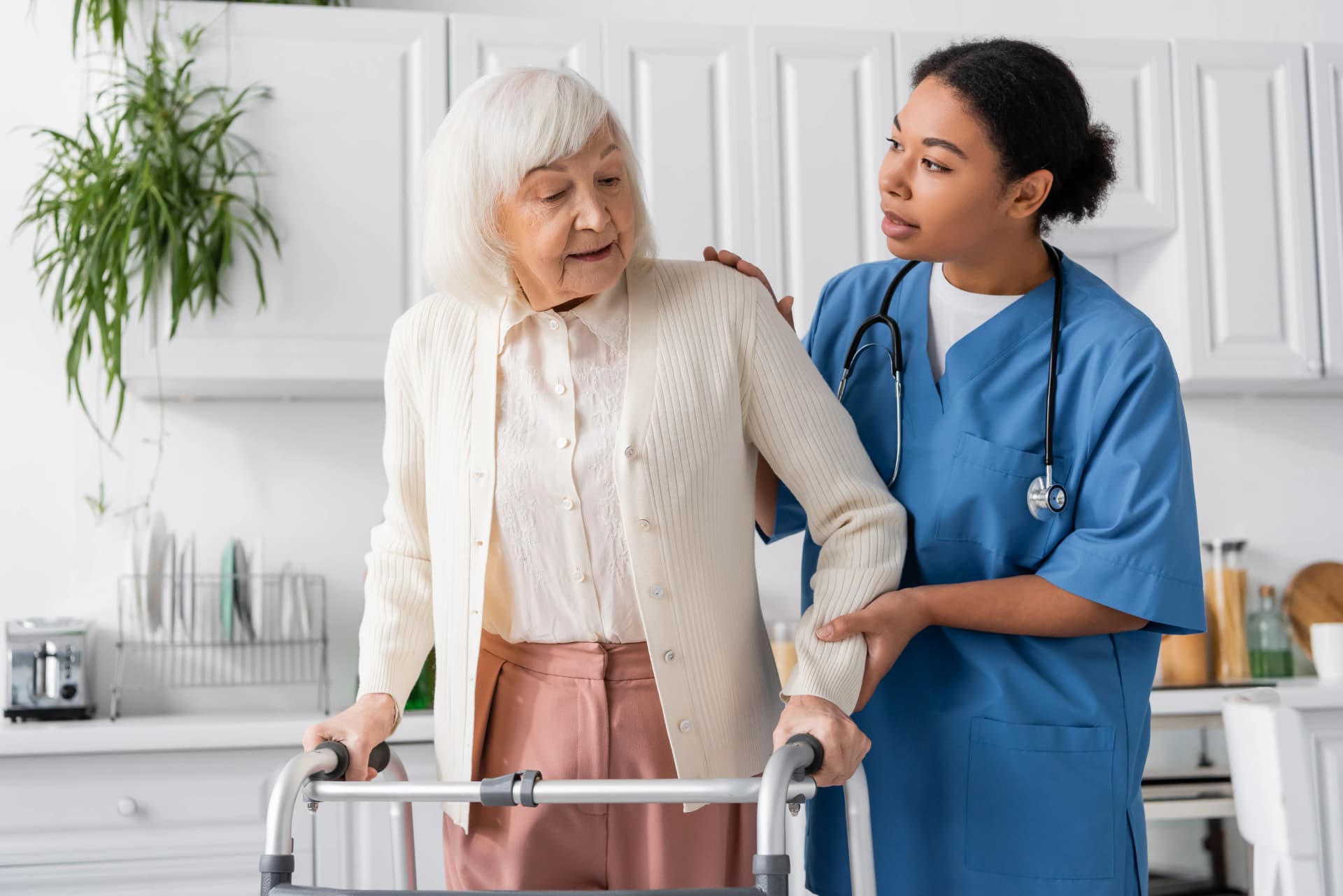 Caregiver helping senior woman stand from couch